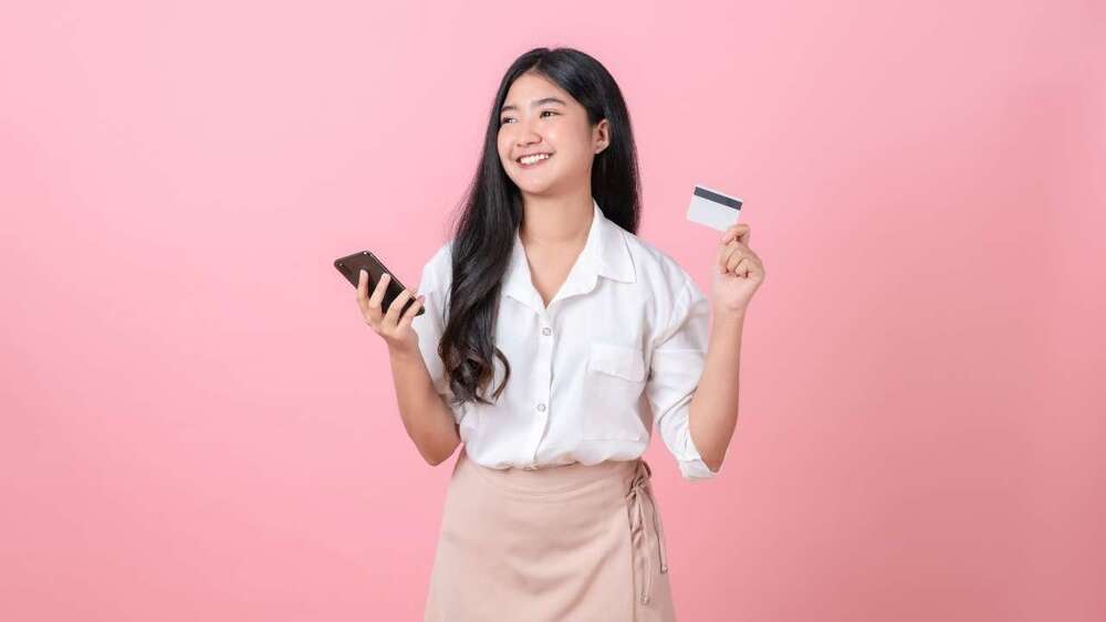 Девушка с телефоном и банковской картой в руках радуется, что ей доступны онлайн займы
